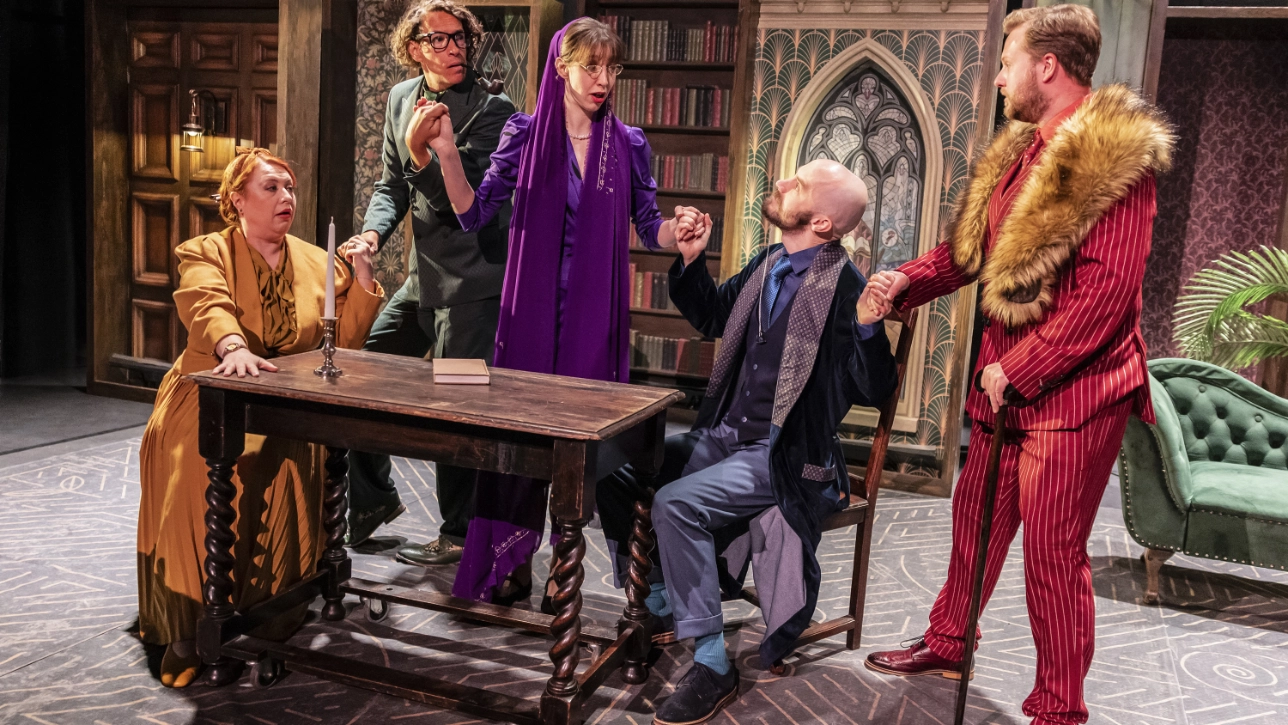 5 actors on stage surrounding a table 