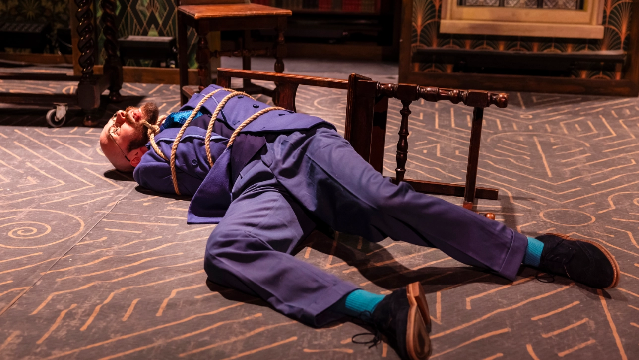 Actor tied to a chair laying on the floor on stage