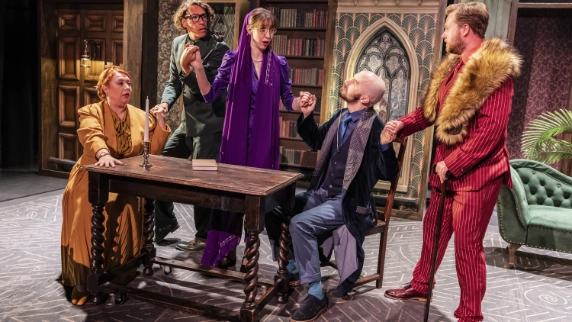 5 actors on stage surrounding a table 