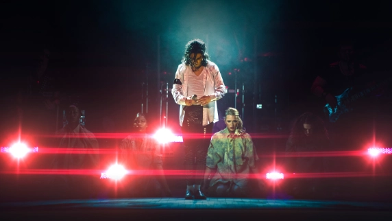 Ben Bowden as Michael Jackson holding a microphone on stage 