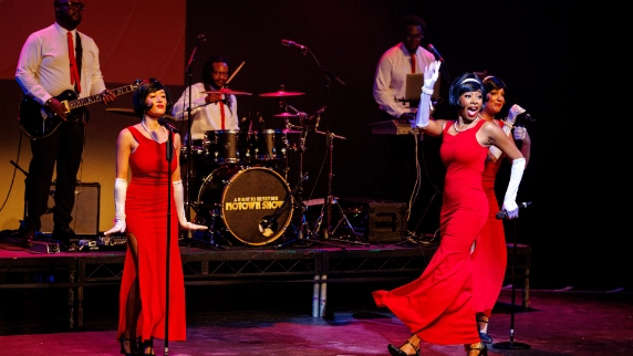 Female motown performers dressed in red gowns with a band behind them