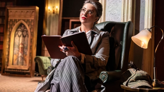 Actor on stage sitting  on a chair holding a book 