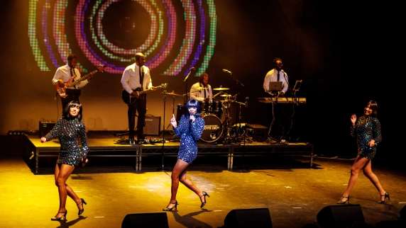 3 female motown performers in sparkly dresses alongside a band