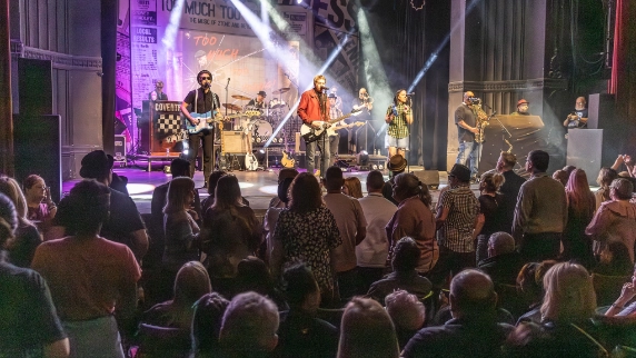 Colour photo of the band Too Much Too Young performing live on stage, viewed from the audience.