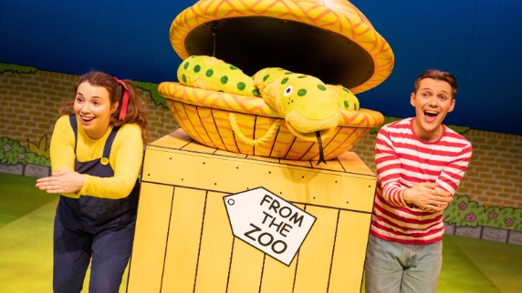 Two performers stand by a colorful crate labeled 