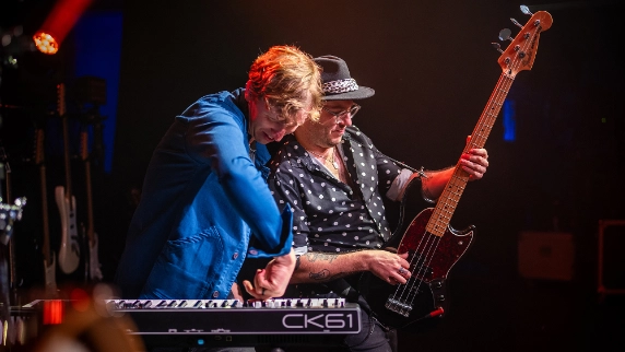 Two musicians performing together on stage - one at keyboard, one playing bass guitar